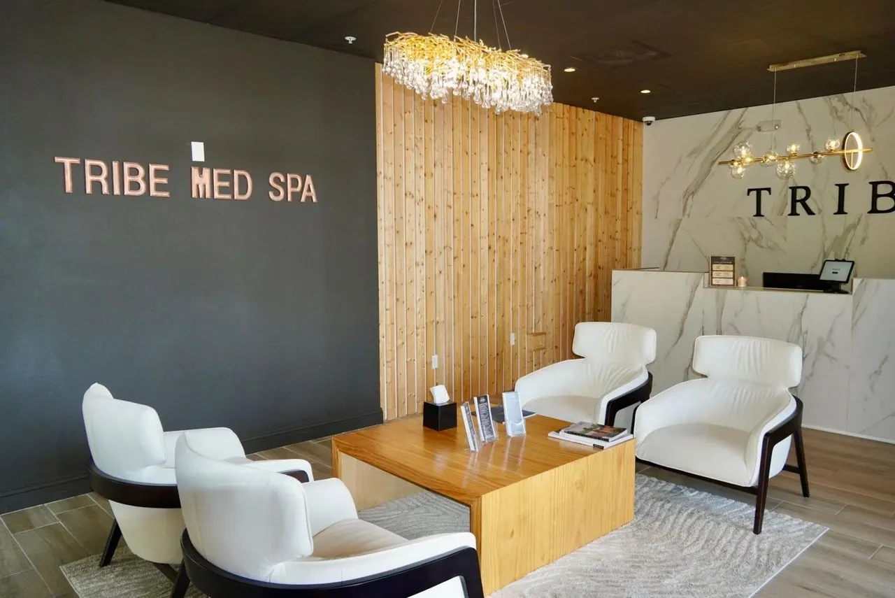 The Tribe Med Spa reception in Naples — pale leather chairs, a timber slat wall and the Tribe Med Spa lettering behind the desk